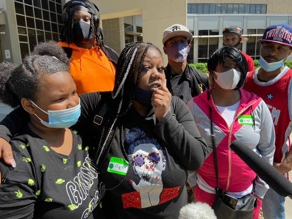 A family, many wearing face masks, gather outside a hospital.