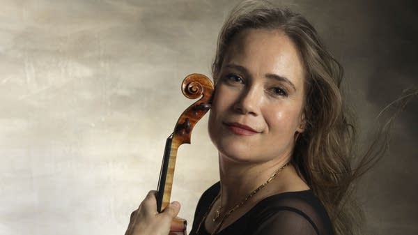 A woman holding a violin poses for a portrait