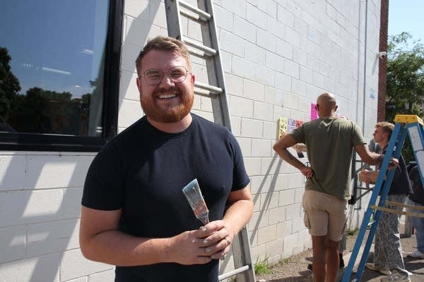 A man smiles while holding a paintbrush.