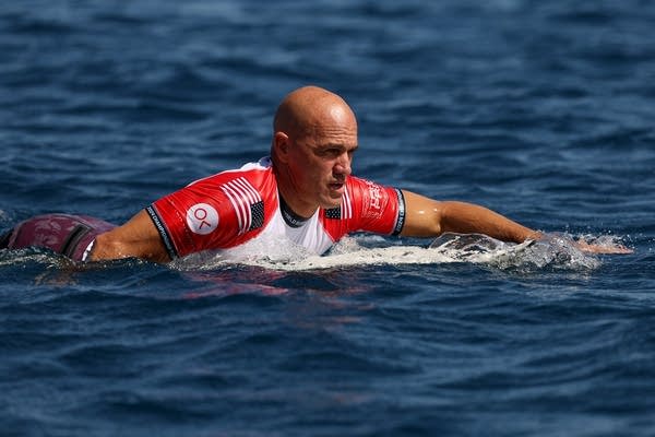 A surfer paddles his board through calm waters