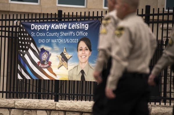 Officers walk past a large banner memorializing a deputy