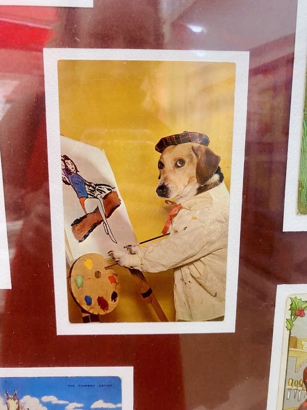 A postcard with a photograph of a dog dressed like an artist and holding a paint brush and palette.