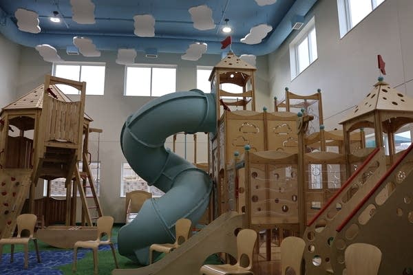 A wide shot of an indoor playground with a green slide in the center.