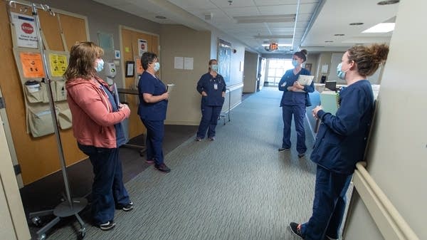 Five women stand in a hallway wearing face masks.