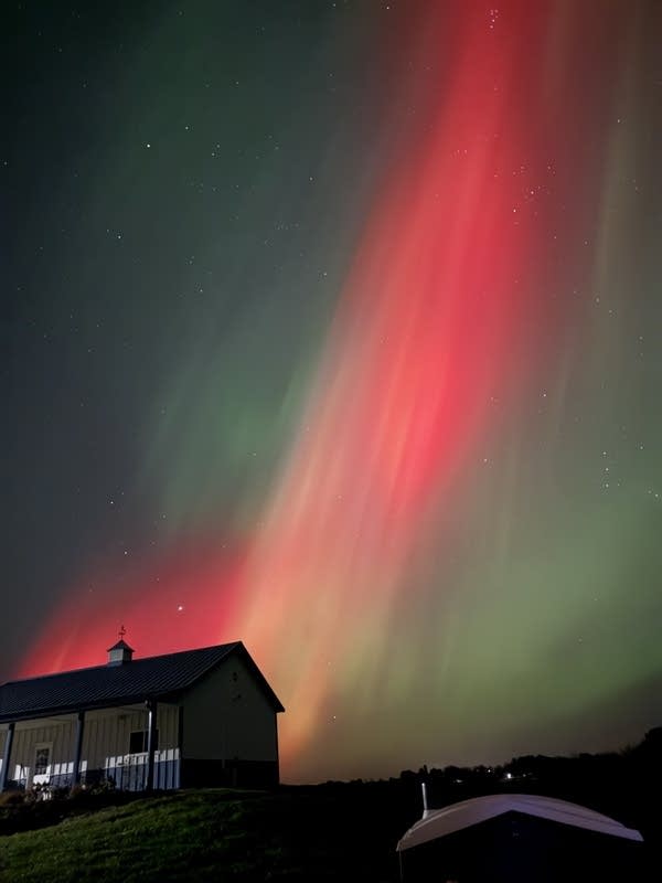A house sits on a hill with the northern lights behind them.
