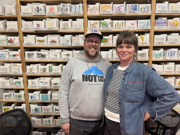 A man and woman stand in front of merchandise on racks of storage.