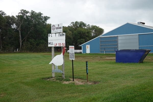 A warning sign in the middle of a clearing with a QR code and a wooden cutout of a turkey.
