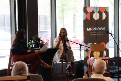 Two women sit on a stage in a library with microphones.