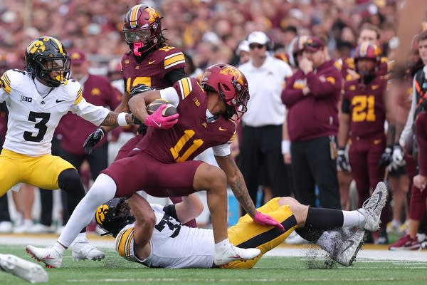 A football player carrying the ball struggles to stay upright after a tackle.