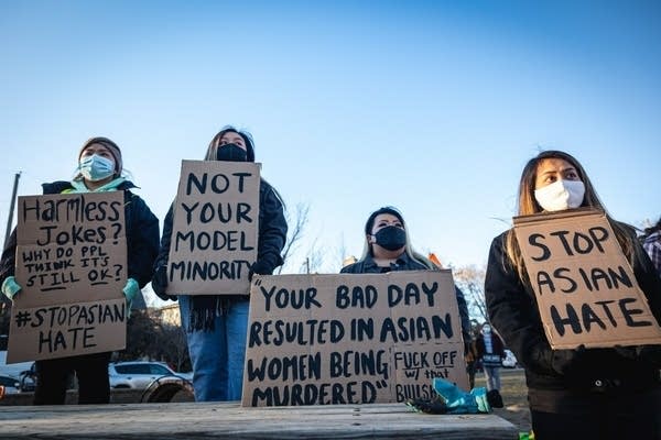 Four people wearing masks hold signs with #StopAsianHate
