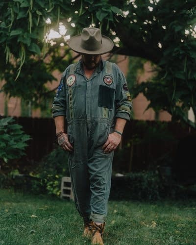 David Huckfelt wears coveralls and stands in a grassy yard.