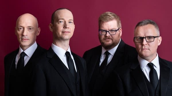 Poster Four men in suits stand together for a studio portrait