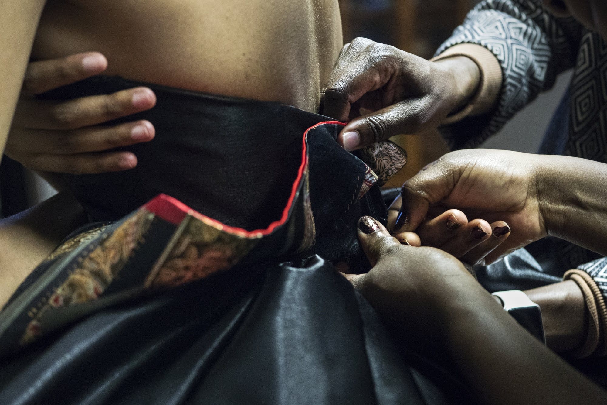 Hands move in to help secure an elaborate dress during fittings.