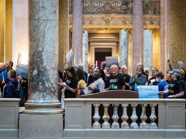 A crowd of people stand among the arches of the capitol