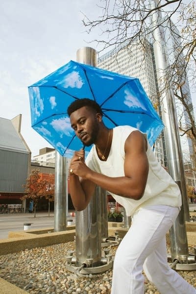 A man leans forward holding a blue umbrella on his shoulder