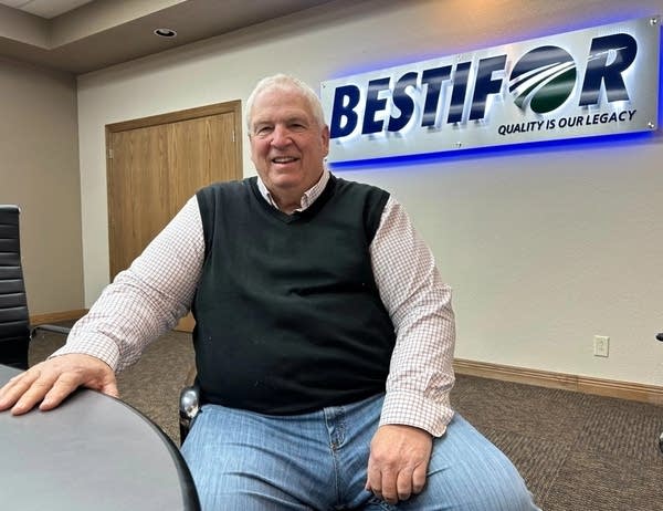 A man sits at a table with a "Bestifor" sign behind him.