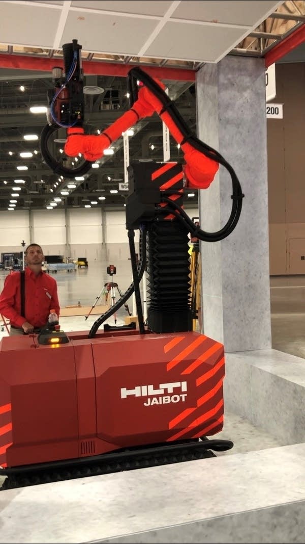 Seen in this photo is the semi-autonomous construction robot, Jaibot, and a man standing next to it and looking at it.