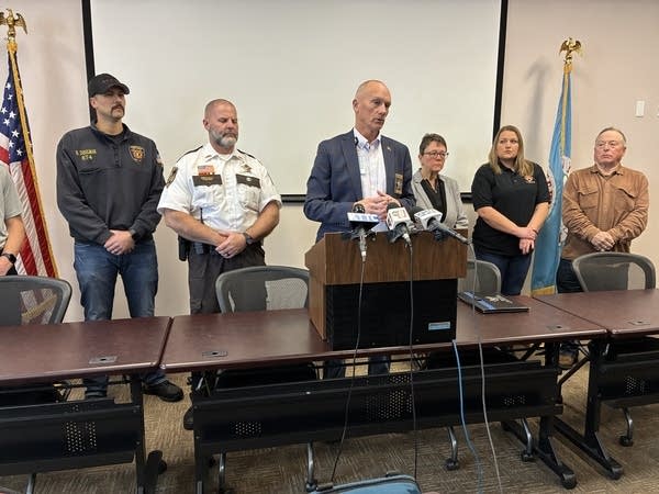 Six people stand behind a table with a podium.
