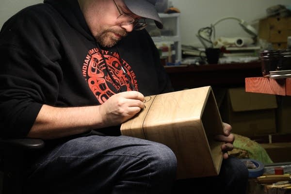 A man in a dark sweatshirt holds a wooden box.