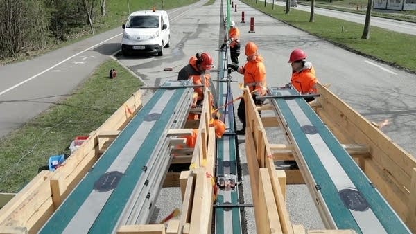 Construction workers are gathered around a green strip being installed into the center of a road.