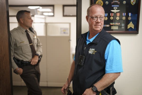 Two police officers stand in an office setting.