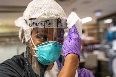 A woman wearing a face shield wipes it clean with sanitizing liquid.