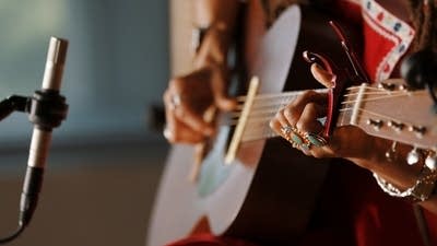 A woman sings and plays guitar in a recording studio