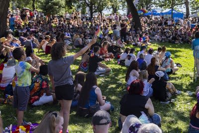 People in a crowded park wave pride flags.