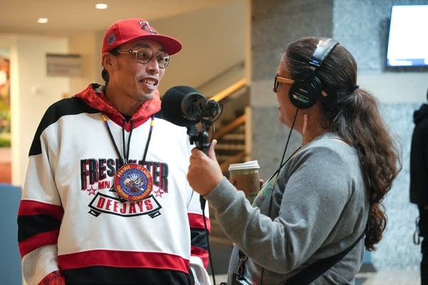 A man gets interviewed by a woman wearing headphones and holding a microphone