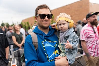 A man in sunglasses holds a baby wearing ear protection