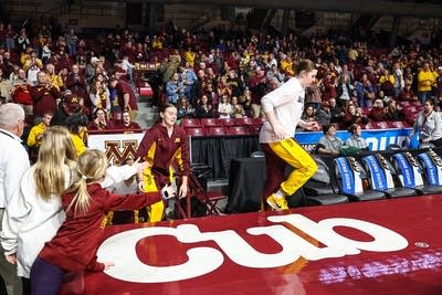 Minnesota women's basketball players run onto the court as fans look on.