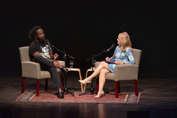 Two people sit on a stage with microphones.