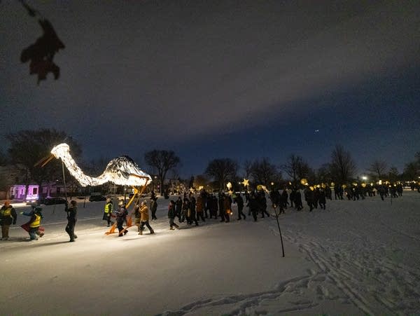 A 25-foot tall heron puppet leads hundreds of community members through the snow in Powderhorn Park in Minneapolis during a winter solstice celebration on Friday, Dec. 20, 2024. 