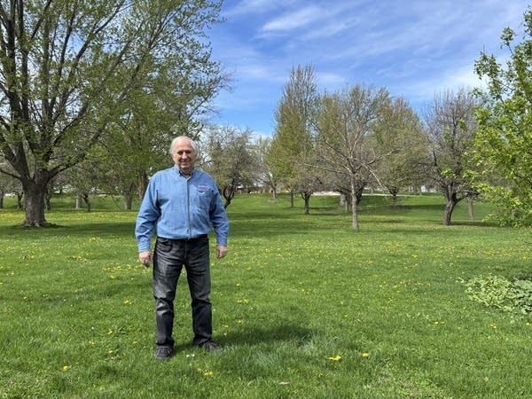 A man stands near a large green space in the city.
