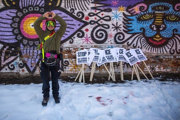 A person stands with signs and makes a heart with their hands