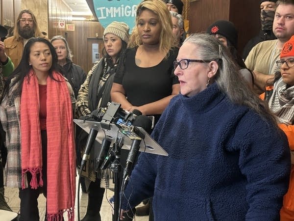 A woman gives a press conference surrounded by people.