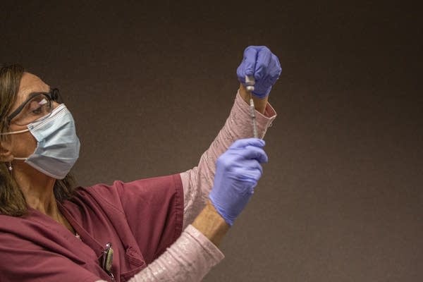 A woman inserts a needle in a vial. 