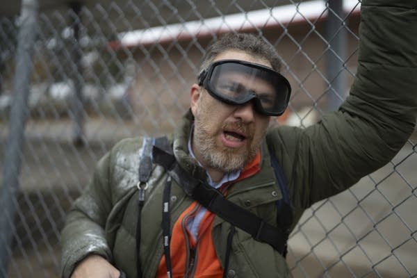 A man wearing goggles rests by a fence