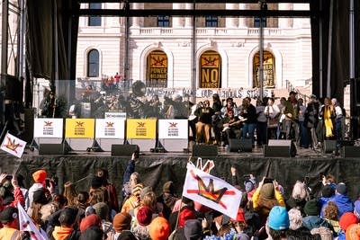 A large group of musicians perform on an outdoor stage at a huge rally