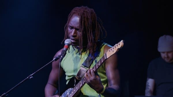 Man with brown dreadlocks strums guitar