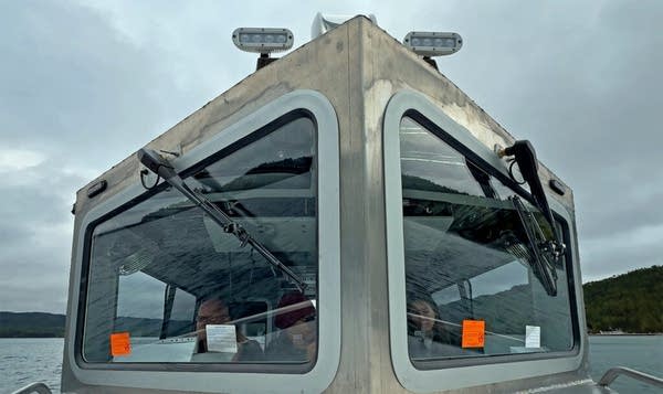Exterior shot of a boat's cockpit. Through the window, three people are seen.