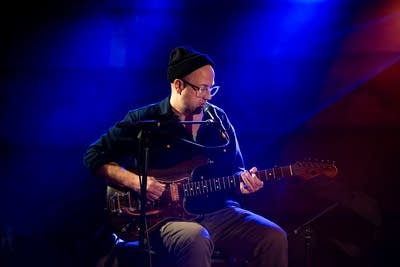A musician sings and plays guitar onstage in a music venue