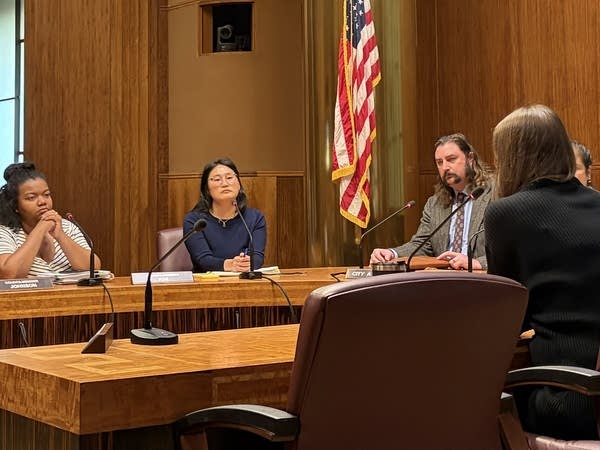 City council members talk around a U-shaped wooden table.