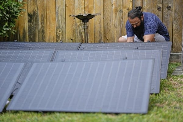 A man crouches down to install solar panels in his yard.