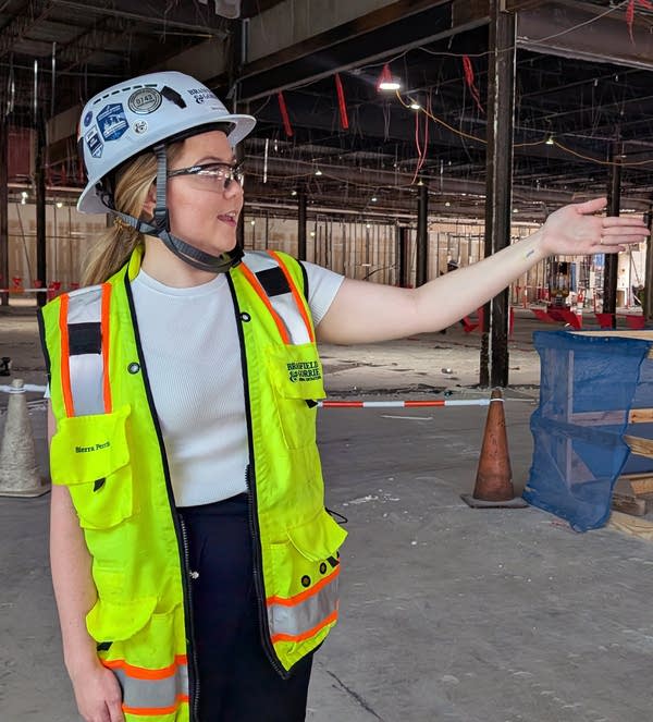 A young white woman in a construction vest and hat points to her left