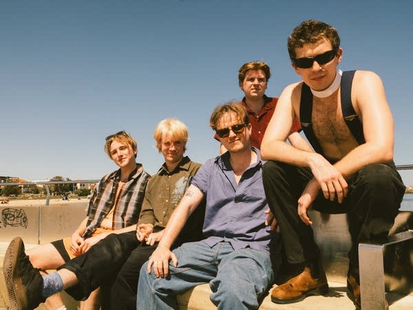 Five men pose for a photo sitting on a bench