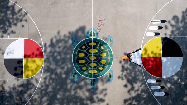 Overhead view of a basketball court, where a mural of a turtle and four-colored circles have been painted.