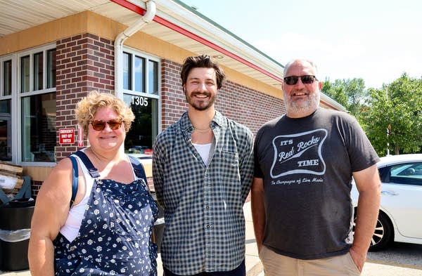 Three people pose for a photograph outside a building.