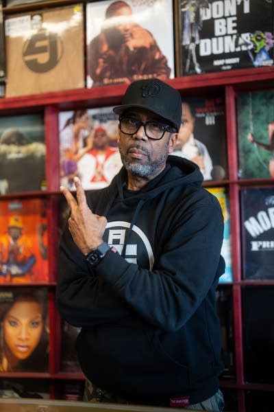 A man poses for a photo while standing in front of a wall of records in the shop he owns
