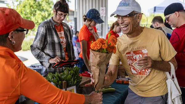 Liz Graznak, owner of Happy Hallow Farm, hands Daniel Kuebler a bouquet after paying for vegetables in Columbia, Missouri. Graznak gave the first 100 customers a free bouquet with their purchase, and the flowers were seen being carried up and down the Columbia Farmers Market.